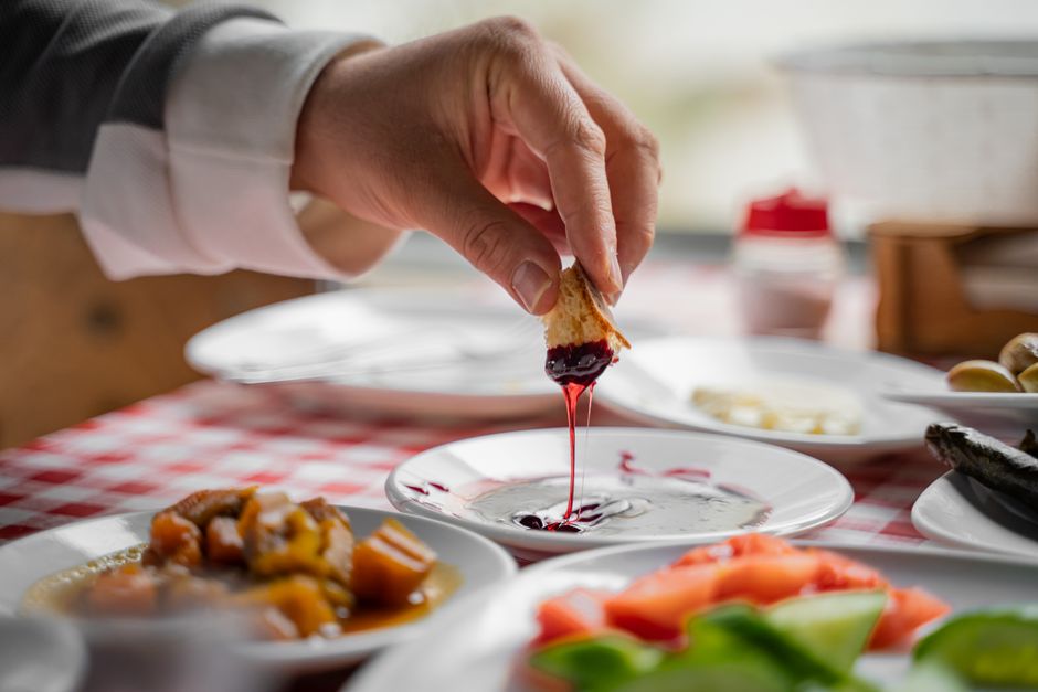 A close-up of a hand dipping bread in jam during a cozy breakfast in Bursa, Türkiye.