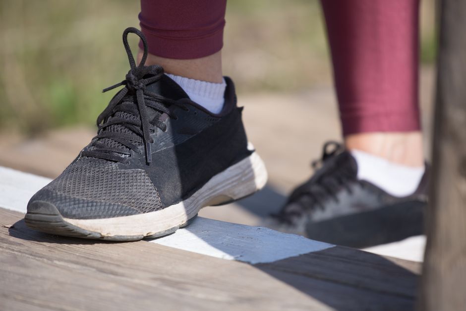 A close-up of black athletic shoes stepping onto outdoor wooden stairs in daylight.