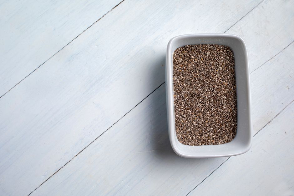 A close-up of chia seeds in a white bowl on a light wooden surface, showcasing a healthy food concept.
