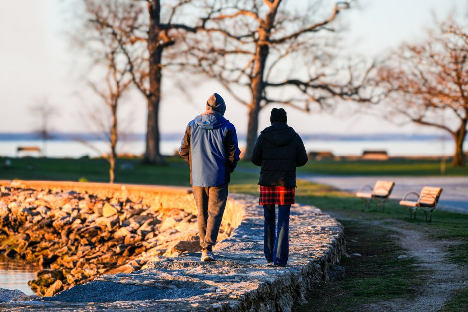 A couple strolls along a rocky path in a serene autumn park by a lake.