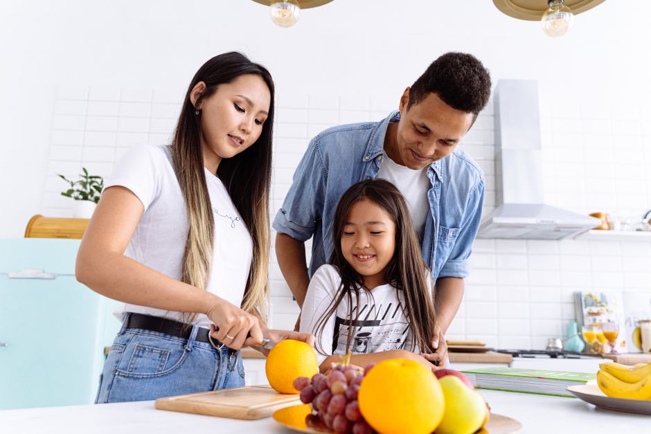 A family joyfully slicing oranges together in the kitchen. Healthy and fresh lifestyle concept.