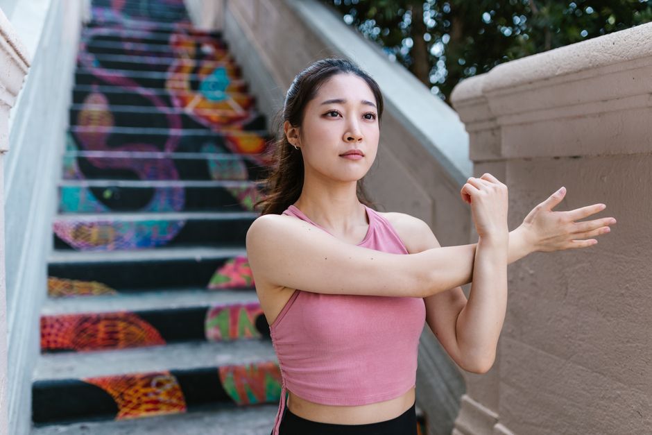 A focused young woman in a pink crop top stretches on colorful graffiti stairs.