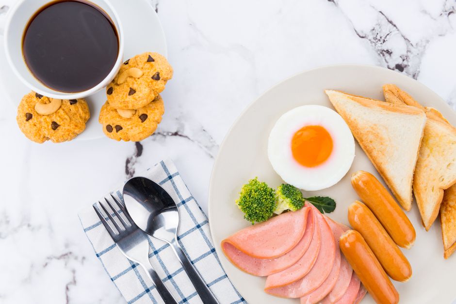 A hearty breakfast of toast, egg, sausages, and coffee on a marble surface.