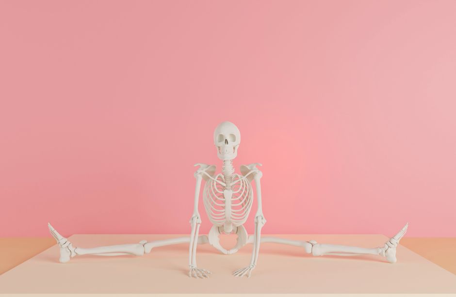 A human skeleton model does a split against a pink backdrop, showcasing flexibility.