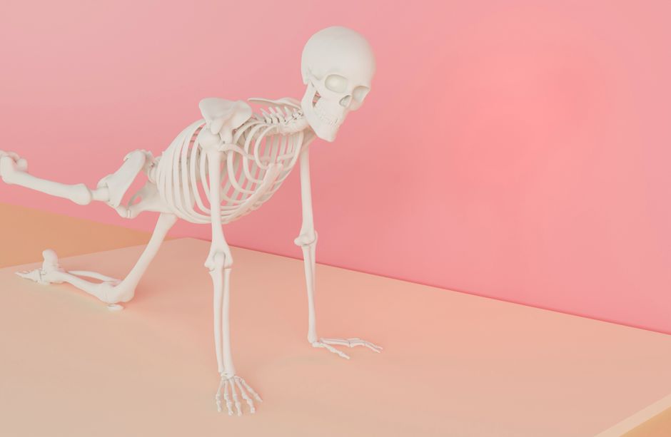 A human skeleton model striking a yoga pose on a pastel pink backdrop in a studio.