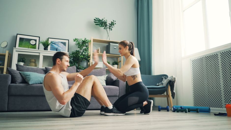 A man and woman exercising together in a living room, focusing on fitness and coordination.