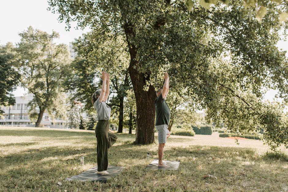 A man and woman practicing yoga outdoors in a sunny park, embodying a healthy lifestyle.