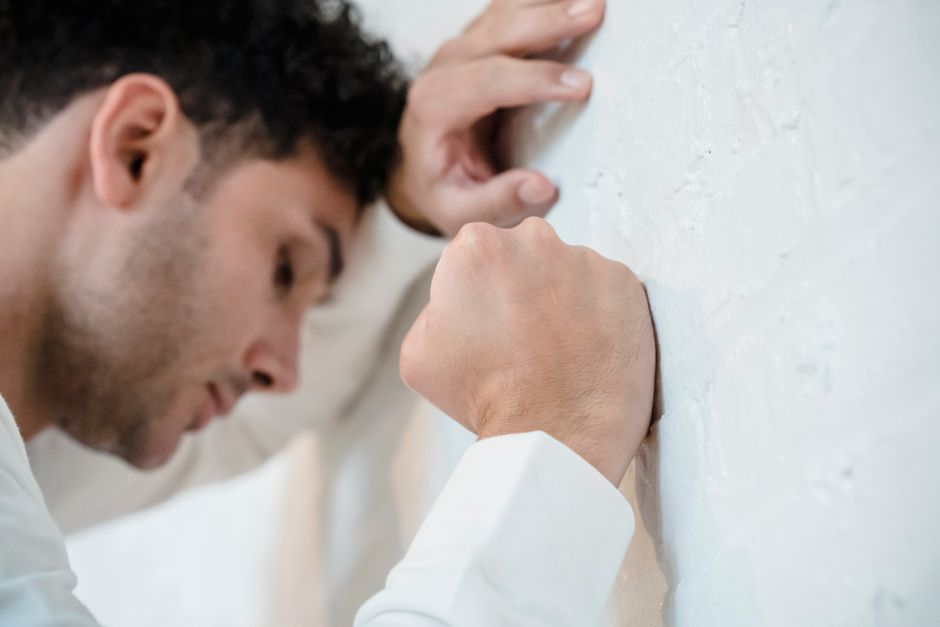 A man in distress leans on a white wall, depicting stress and anxiety.