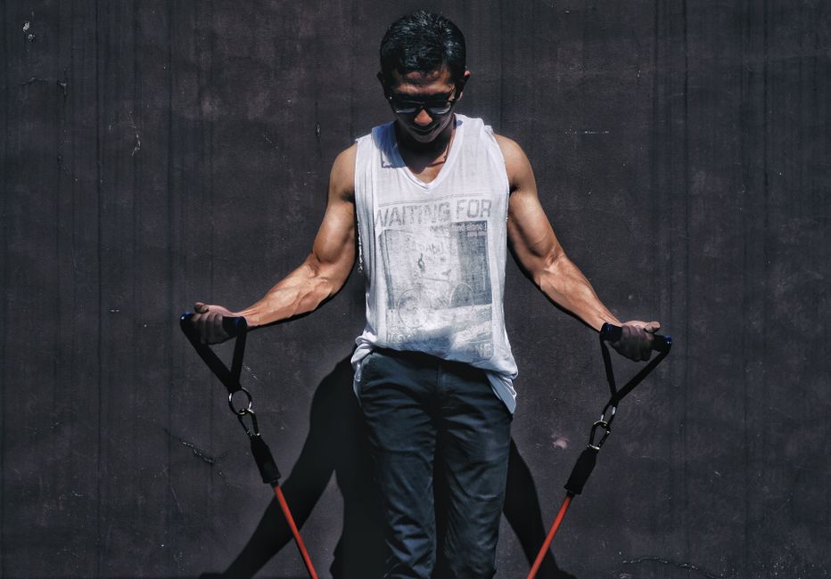 A muscular man using resistance bands outdoors for a fitness workout.