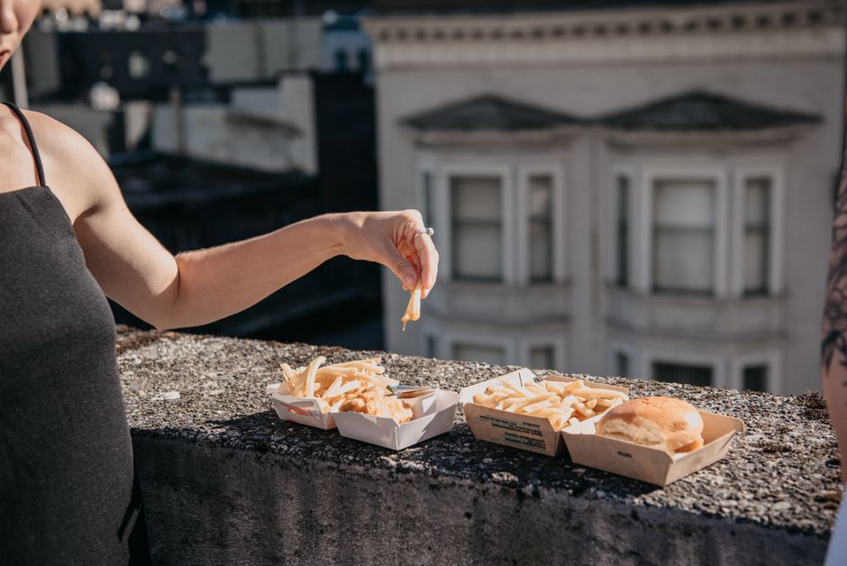 A person enjoying fries and a burger on an urban rooftop during the day.