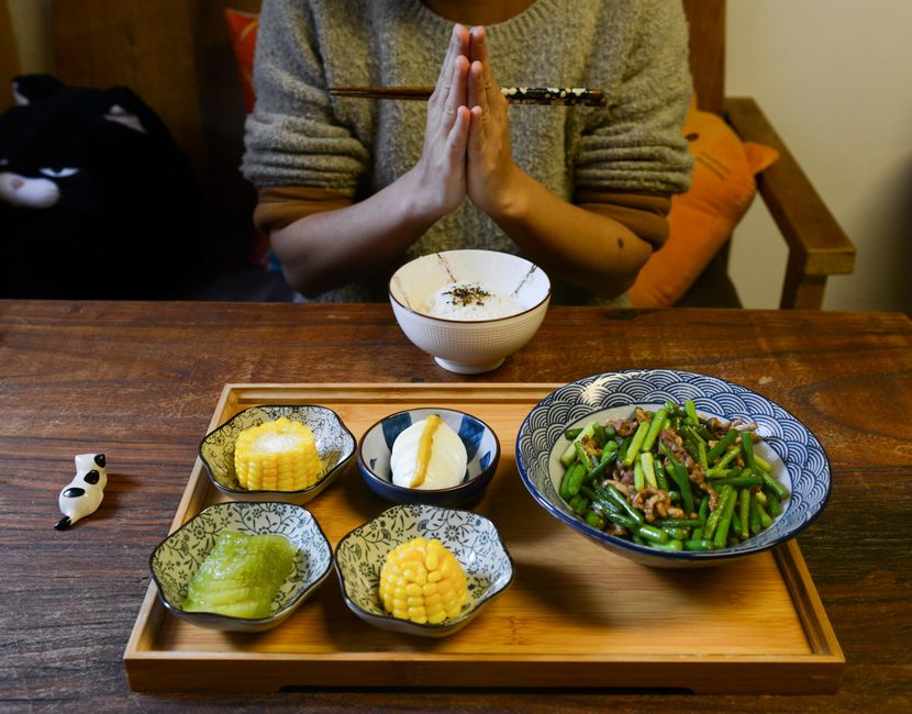 A person prays before enjoying a homemade Asian meal featuring vegetables and rice.