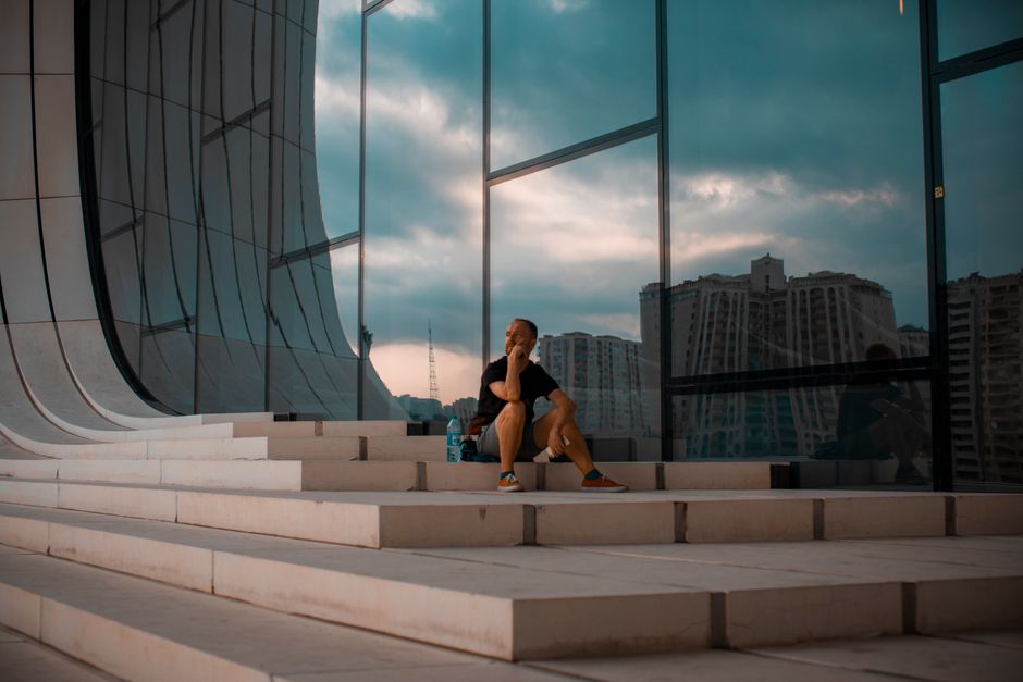 A person sits thoughtfully on steps while skyscrapers reflect on glass in Baku, Azerbaijan.