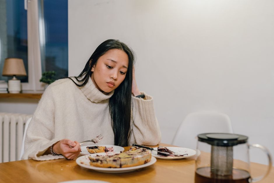 A thoughtful woman in a cozy sweater eats dessert alone, reflecting deep thoughts.