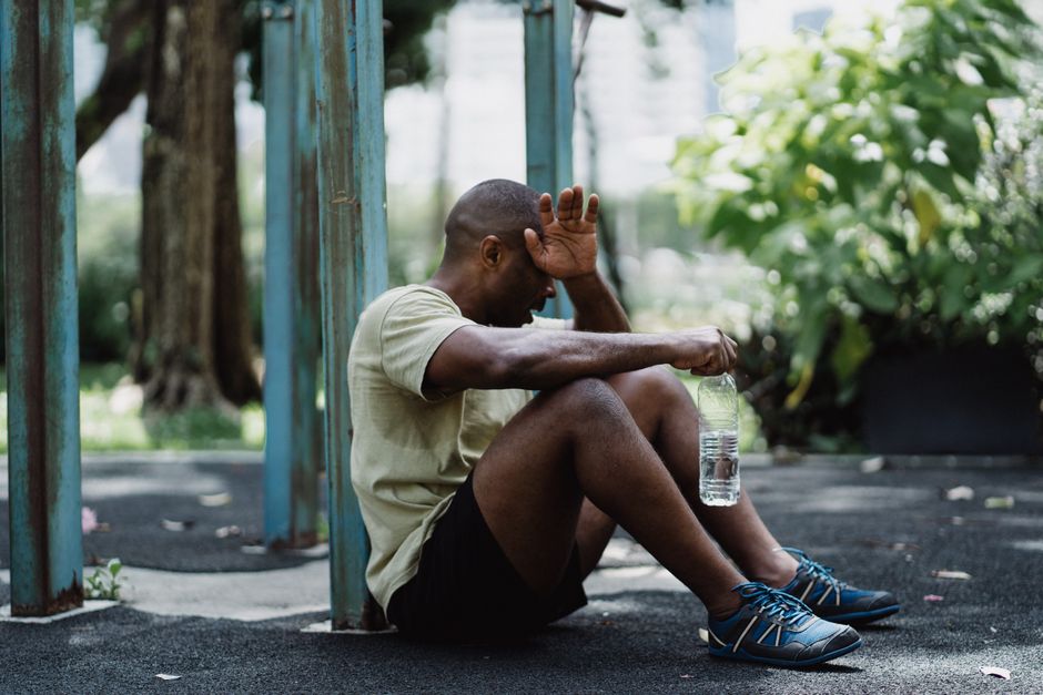A tired man takes a break from exercise sitting on the ground with a water bottle in hand.