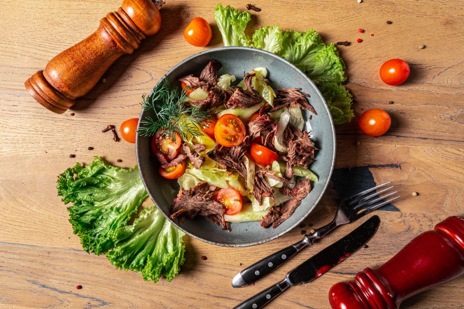 A vibrant grilled meat salad with fresh vegetables and herbs on a wooden table.
