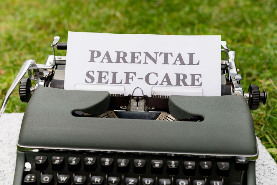 A vintage typewriter showcasing a "Parental Self-Care" message on paper outdoors.