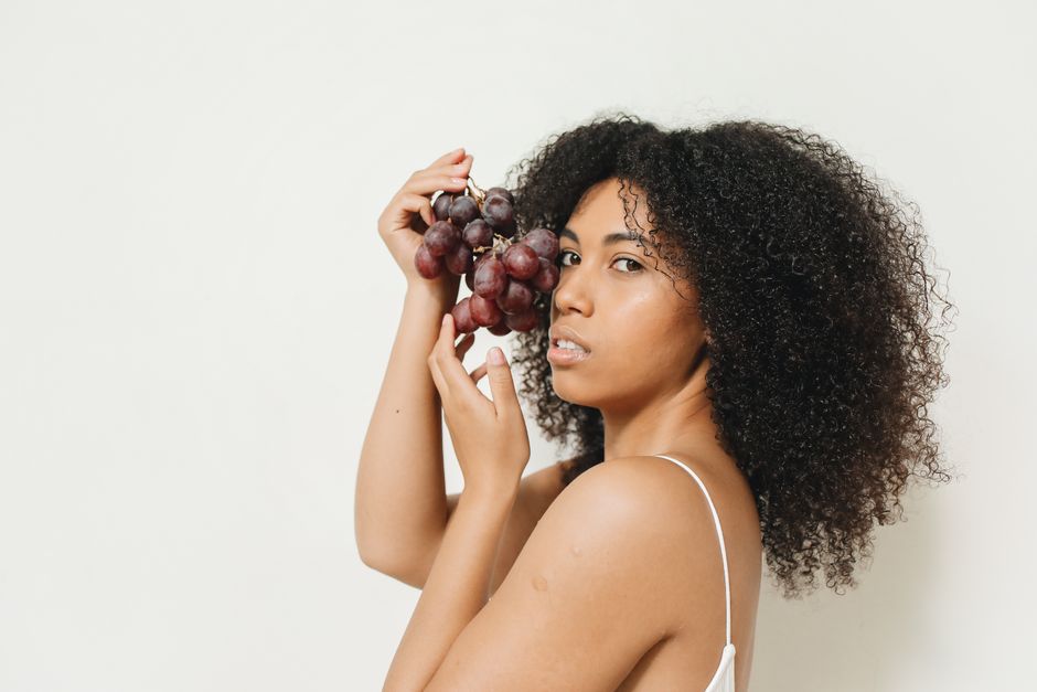 A woman holding grapes against a white background, captured in a studio setting.