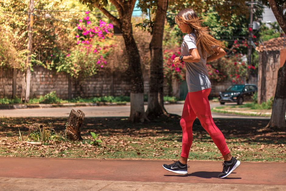 A woman jogs on a path surrounded by trees and vibrant flowers, embodying a healthy lifestyle.