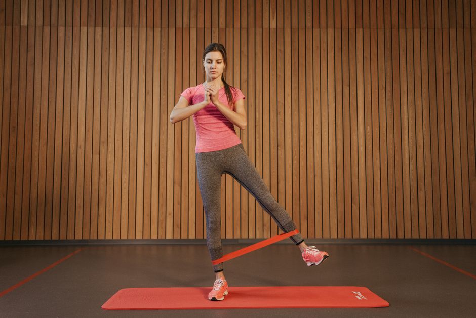 A woman performs leg exercises with a resistance band at a gym, promoting fitness and healthy living.