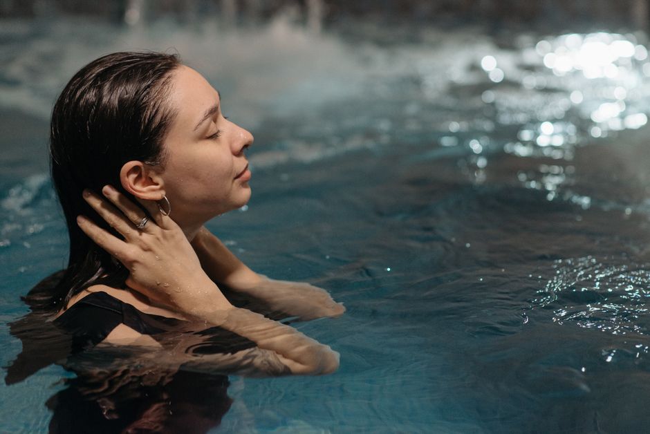 A woman relaxes with eyes closed in a nighttime swimming pool setting, enjoying tranquility.