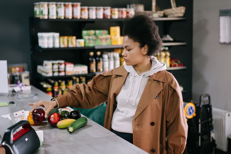A woman selecting fresh fruits and vegetables at a grocery store with shelves stocked in the background.