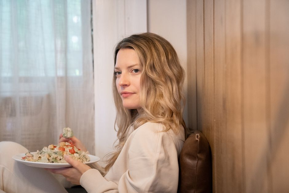 A woman with blonde hair enjoys a healthy salad while sitting at home indoors, exuding comfort and relaxation.