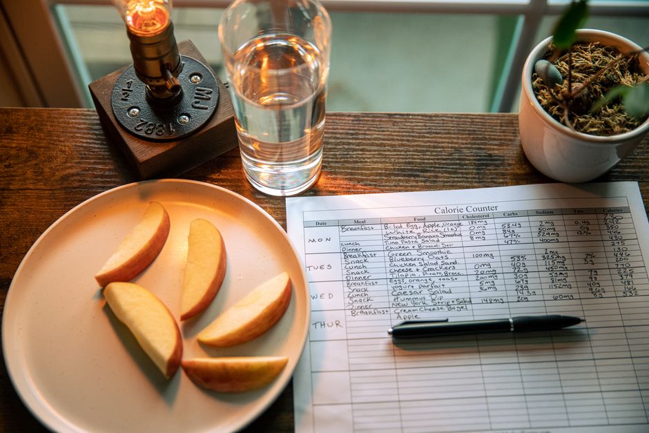A wooden table setup with apple slices, a calorie chart, and a glass of water for a healthy diet plan.