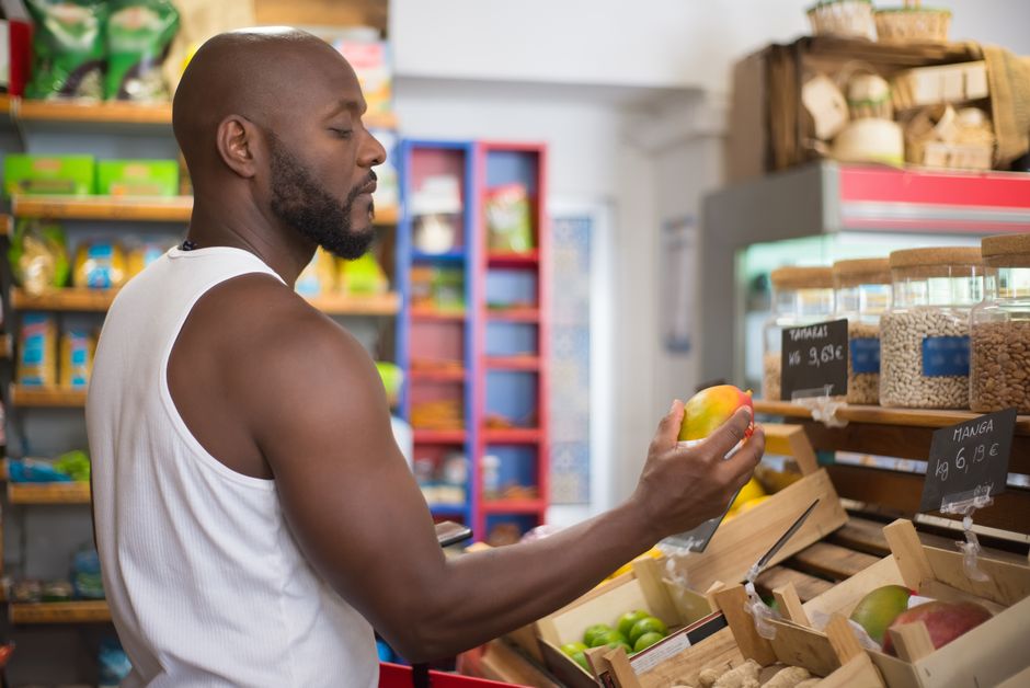Adult man shopping for mangoes in a Portuguese supermarket, examining fruit quality.