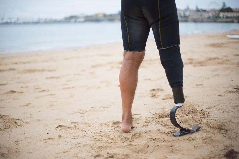 Adult walking on sandy beach with a prosthetic leg, promoting strength and resilience.