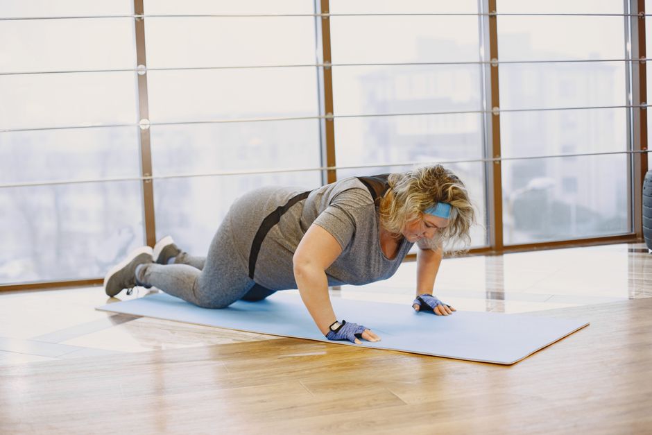 Adult woman doing push-ups indoors on a yoga mat, embracing a healthy lifestyle.