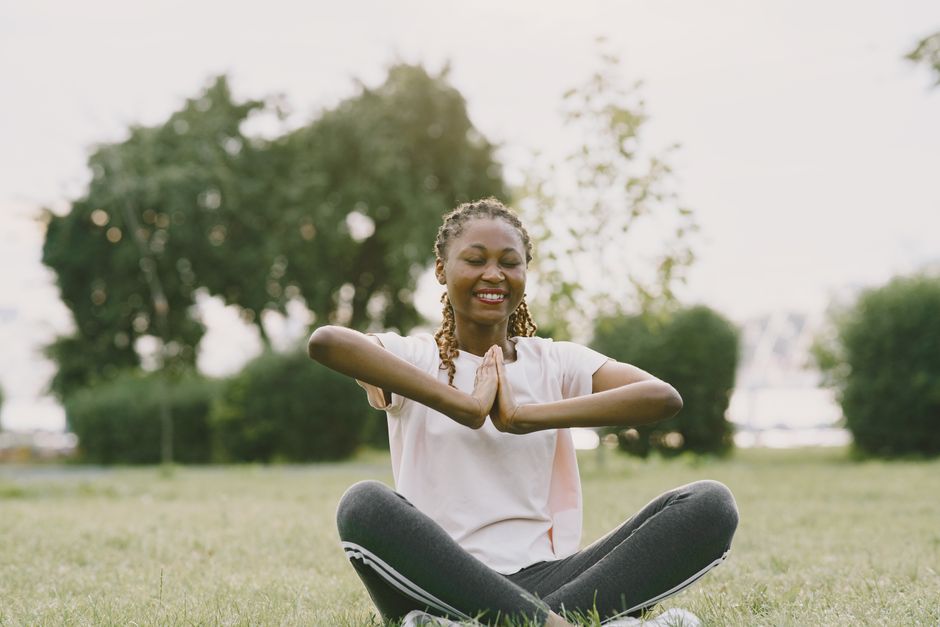 African American woman practicing yoga in a sunny park, enjoying relaxation and wellness outdoors.