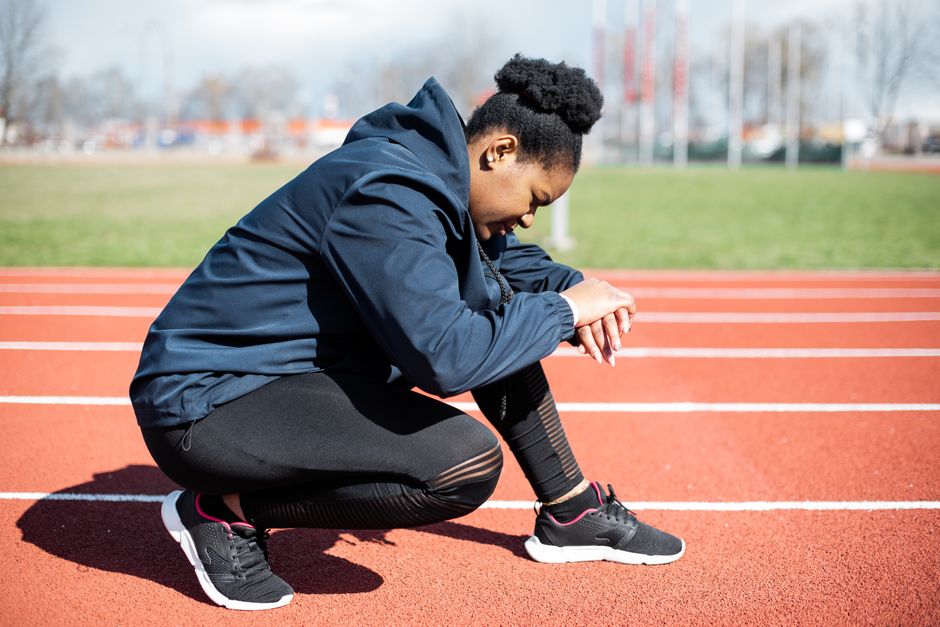 African American woman taking a break on a sunny day on a running track, showcasing fitness and determination.