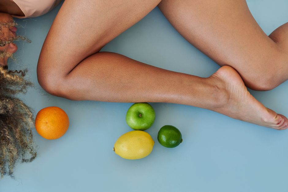 Artistic top-down view of legs with citrus fruits on a blue studio background.