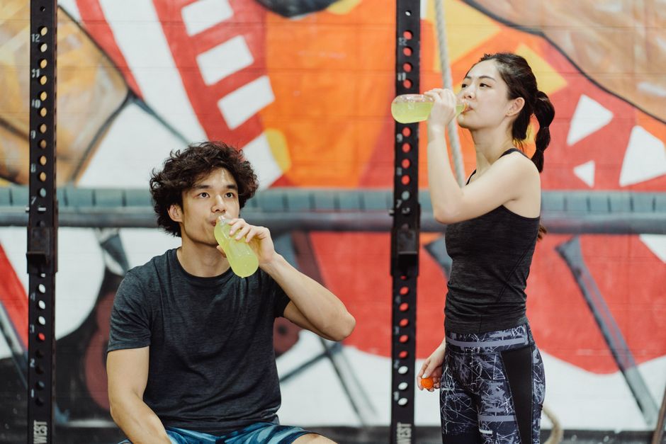 Asian couple in activewear drinking yellow beverages at an indoor gym.