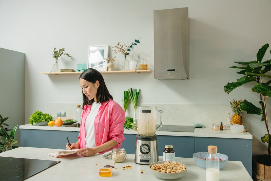 Asian woman writing in a notebook while cooking in a stylish kitchen.