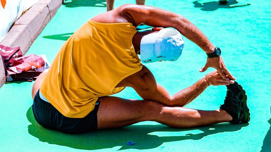 Athletic man stretches on a vibrant outdoor sports court, focusing on flexibility and fitness.