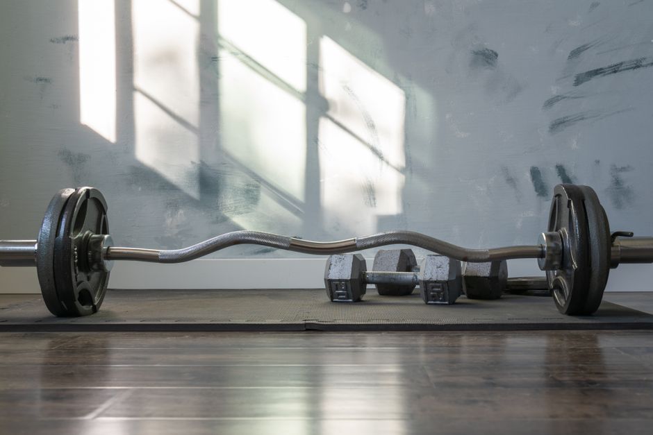 Barbell and dumbbells indoors on a gym mat with sunlight streaming through the window.