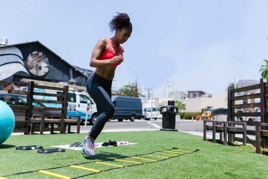 Black woman performing fitness exercises using agility ladder outdoors