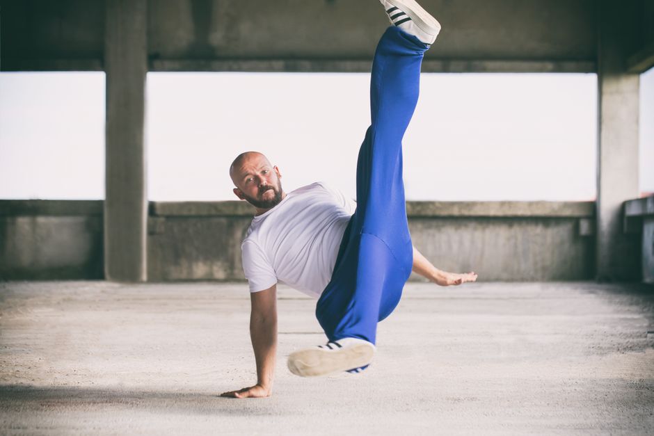 Breakdancer in blue pants showcases a dynamic flair move indoors, emphasizing motion and agility.