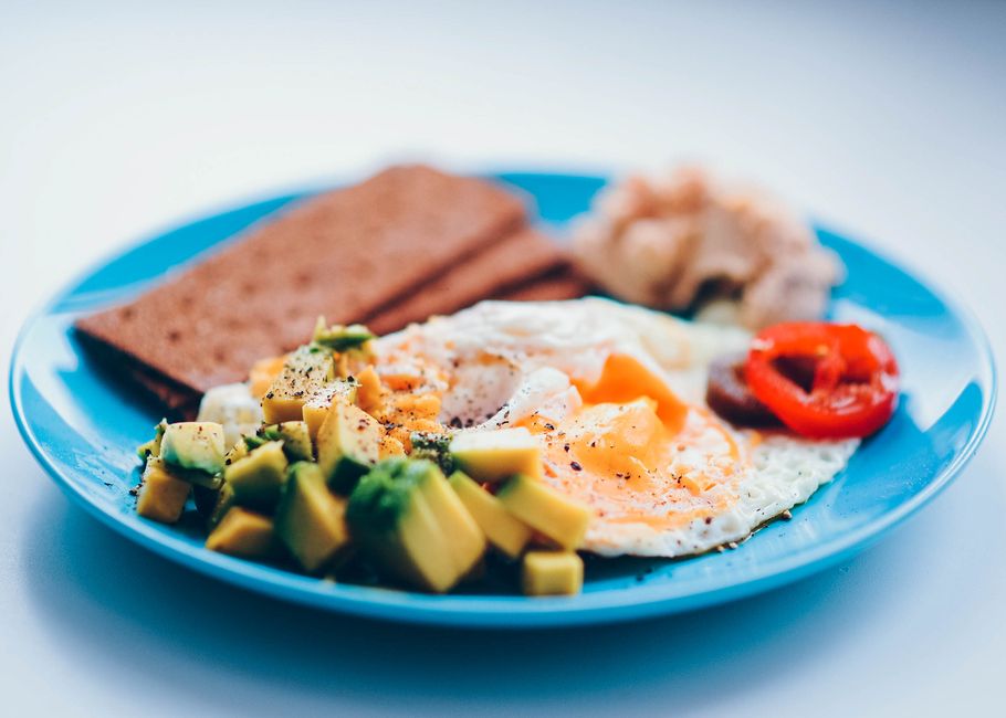 Bright and colorful breakfast featuring fried eggs, avocado, and fresh vegetables on a blue plate.