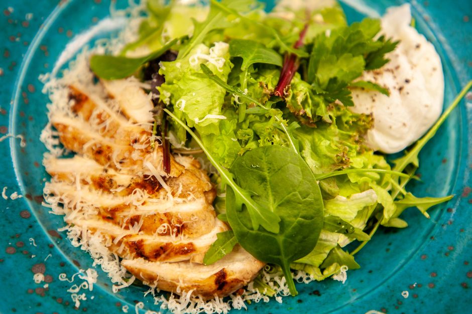 Close-up of a grilled chicken salad with mixed greens and cheese, served on a blue plate.