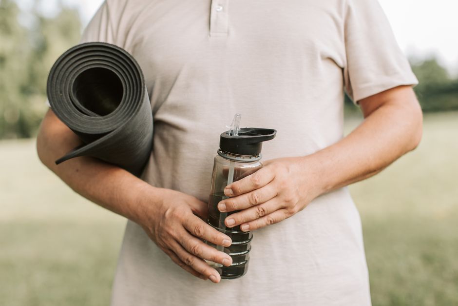 Close-up of a man holding a yoga mat and water bottle, ready for outdoor exercise.