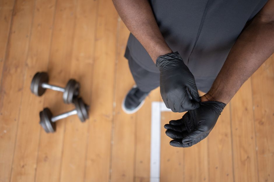 Close-up of a man in gloves standing next to dumbbells on a wooden floor.