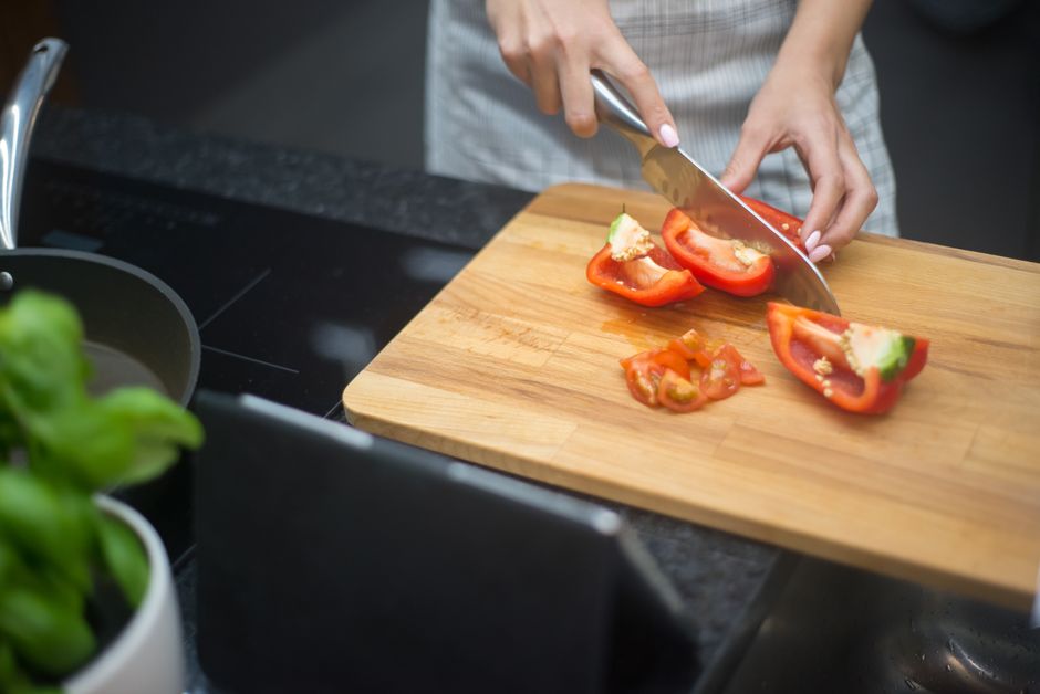 Close-up of a woman slicing red bell pepper in a modern kitchen setting.