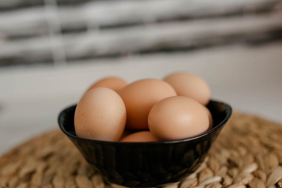 Close-up of brown eggs in a black ceramic bowl on a woven mat, perfect for culinary themes.