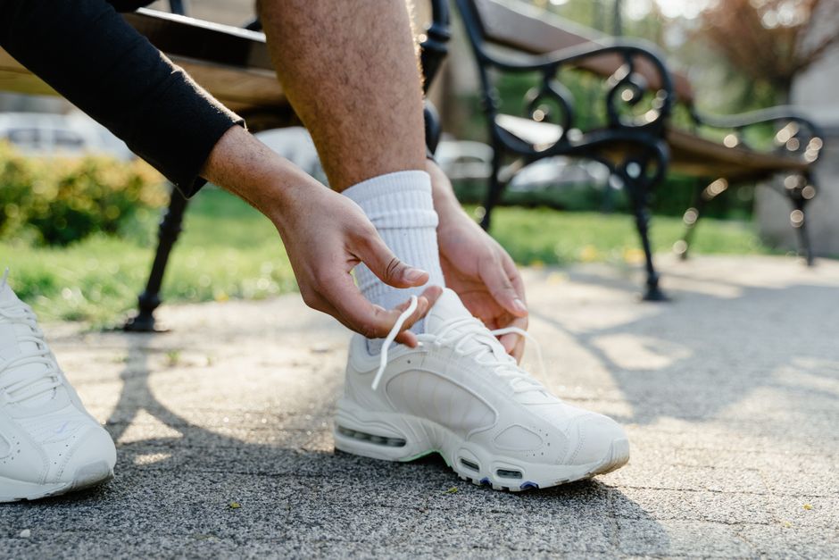 Close-up of hands tying white sneakers in a park setting. Perfect for fitness and lifestyle themes.