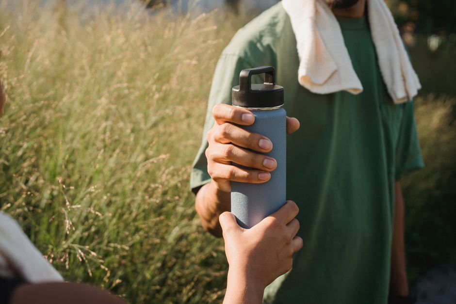 Close-up of two hands exchanging a water bottle in a grassy area post-exercise.