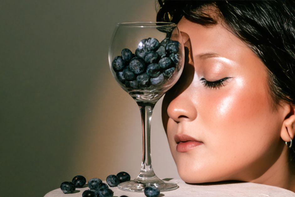 Close-up portrait of a woman alongside a glass filled with blueberries, capturing elegance and creativity.