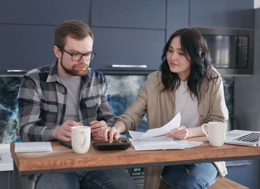 Couple sitting at home managing finances with documents and calculator.
