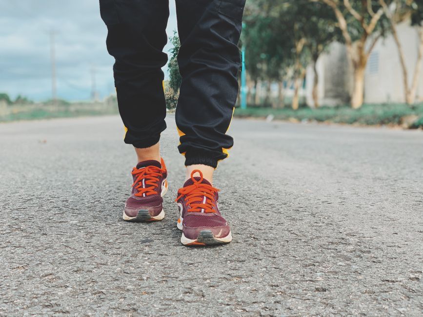 Crop legs of person in sneakers and sportswear standing on asphalt road on blurred background of green trees in countryside